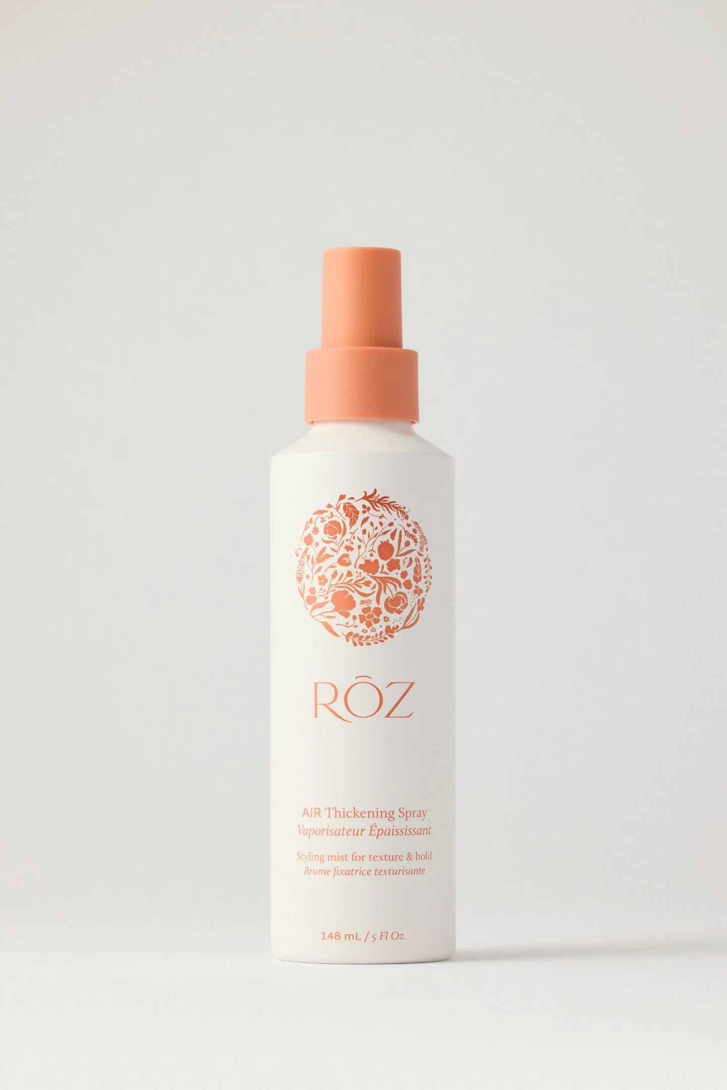White spray bottle with orange nozzle of ROZ thickening spray on a light gray background