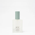 Clear bottle of ROZ Santa Lucia styling oil with green top on white background